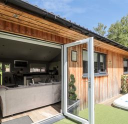 An open door leads from a wooden cabin to a living room with a sofa and kitchen inside at Lodge 32 Otterburn