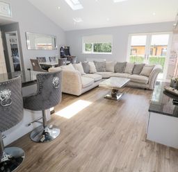 A living room with an L shaped sofa a marble coffee table bar stools and a dining area at Lodge 32 in Otterburn