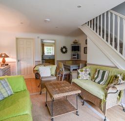 A living room with wicker sofas and chairs a coffee table a dining table and staircase at 52 Fernhill Heights in Charmouth