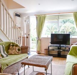 A living room with wicker sofas and a small table a television on a stand and an open door at 52 Fernhill Heights in Charmouth
