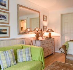 A living room with green sofa cushions a wicker chair lamps on a wooden sideboard and framed pictures on the wall at 52 Fernhill Heights in Charmouth