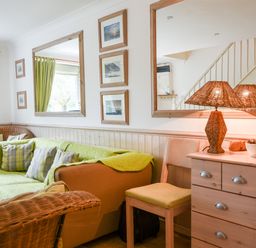 A living room with green curtains sofas wicker chair and a wooden dresser with a lamp at 52 Fernhill Heights in Charmouth