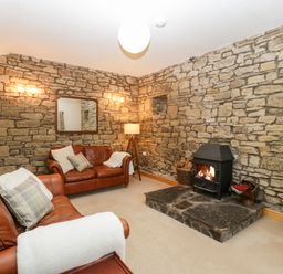 A living room with two brown leather sofas a stone fireplace a wooden TV stand and a mirror on a stone wall at Bullfinch Cottage in Kingsland