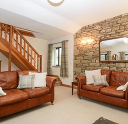 A living room with two brown leather sofas, a stone wall with a mirror, and wooden stairs at Bullfinch Cottage in Kingsland