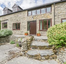Stone cottage exterior with wooden door stone steps and shrubs at Bullfinch Cottage in Kingsland