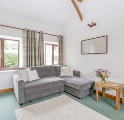 A living room with a grey sofa cushions wooden side table and flowers at Fieldfare in Kingsland