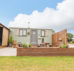 An outdoor area with a small green cabin wooden fencing and garden furniture at Heather Hut at Copy House Hideaway in Earby