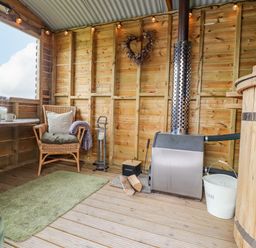 A wooden room with wicker chairs a table a small stove logs and a hot tub at Heather Hut at Copy House Hideaway in Earby