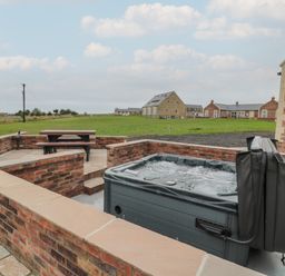 An outdoor patio with a hot tub and a picnic table surrounded by brick walls at Whinny Cottage in Embleton