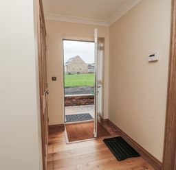 A hallway with wooden floor a partially open door and a black mat at Whinny Cottage in Embleton