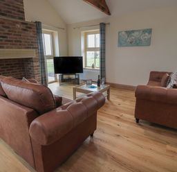 A living room with two brown sofas a TV on a stand a wooden coffee table with wine and glasses and a brick fireplace at Whinny Cottage in Embleton