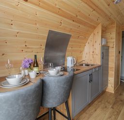 A kitchenette with two dining chairs plates bowls glasses a kettle and a sink in a wooden pod at Dysynni Pod in Llanegryn near Tywyn