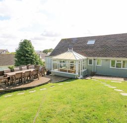 A backyard with a wooden deck and outdoor dining table next to a house with a conservatory at Treestumps in Benllech