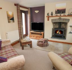 A living room with plaid sofas a wooden coffee table and a fireplace with a wood stove at 2 Yr Hen Felin in Castle Morris near Letterston