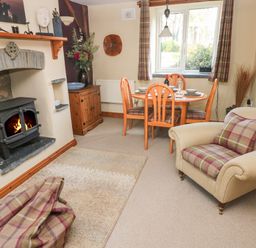 A living room with a wood stove fireplace dining table with four chairs and an armchair at 2 Yr Hen Felin in Castle Morris near Letterston