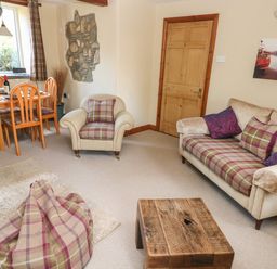 A living room with a sofa armchair dining table wooden door and a wooden coffee table at 2 Yr Hen Felin in Castle Morris near Letterston