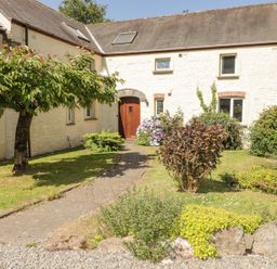 A stone cottage with a wooden door and garden with trees and shrubs at 2 Yr Hen Felin Castle Morris near Letterston