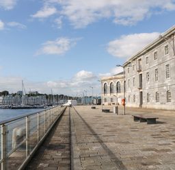 A waterfront promenade with stone paving benches and a stone building next to a marina with boats and yachts at Clarence Riverside Royal William Yard in Plymouth
