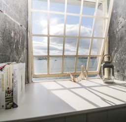 A white window sill with books on the left and a lantern on the right with a view of water through a grid window at Clarence Riverside Royal William Yard Plymouth