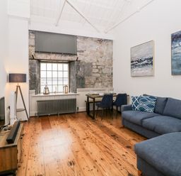 A living room with a blue sofa a wooden floor a television and a dining table at Clarence Riverside Royal William Yard Plymouth