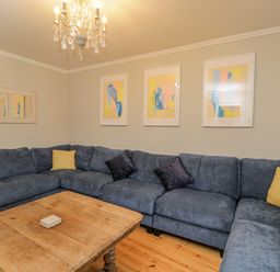A living room with a large blue sectional sofa and wooden coffee table with a chandelier above at White Roses in Whitchurch near Monmouth