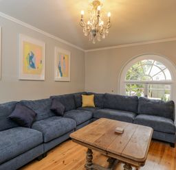 A living room with a blue sectional sofa wooden coffee table chandelier and arched window at White Roses in Whitchurch near Monmouth
