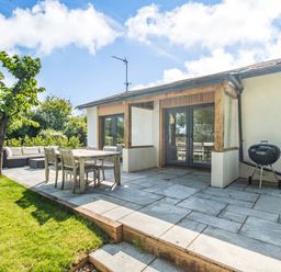 A patio with a wooden dining table and chairs a barbecue and an outdoor sofa next to a garden at The Paddock in Honington near Shipston-On-Stour