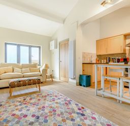 An open living room and kitchen area with a sofa table lamp colorful rug stools and kitchen cabinets at The Paddock in Honington near Shipston-On-Stour