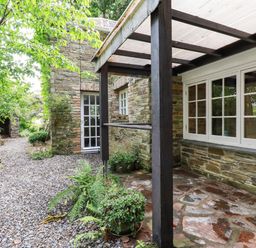 A stone patio with potted plants and a covered porch next to a gravel path and stone building at The Cottage in St Kew