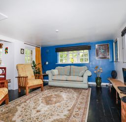 A living room with a striped sofa and armchairs a wooden bench a TV on a wooden stand and plants at The Cottage in St Kew