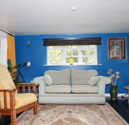A living room with a sofa an armchair a rug and blue accent wall at The Cottage in St Kew