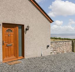 A wooden front door with side window lights on a pebble driveway beside a stone wall and countryside at Little Barn in Grange-Over-Sands near Cartmel