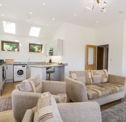 An open plan living room and kitchen with beige sofas washing machine and dining table at Little Barn in Grange-Over-Sands near Cartmel