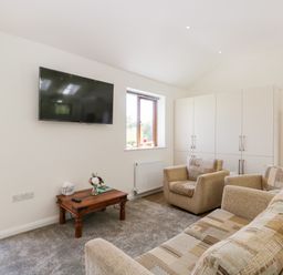 A living room with a sofa, armchairs, coffee table, wall-mounted TV, and cupboards at Little Barn in Grange-Over-Sands near Cartmel