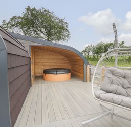 An outdoor deck area with a covered hot tub and a cushioned hanging chair at Laird Lodge 1 in Lochmaben