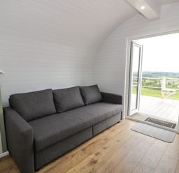 A room with a grey sofa wooden floor and an open door leading to an outdoor area at Laird Lodge 1 in Lochmaben