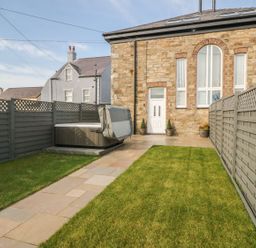 A fenced backyard with grassy areas and a paved path leading to a door on a stone building with large windows at Sardis Chapel 1 Malltraeth