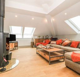 A living room with a wood stove a sectional sofa with cushions and a wooden coffee table at Sardis Chapel 1 in Malltraeth