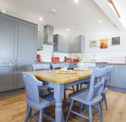 A kitchen with gray cabinets, wooden table with blue chairs, red appliances, and wall art at Escape To The Chapel Anglesey Bryngwran near Rhosneigr