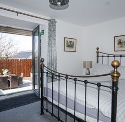 A bedroom with a black metal bed frame and striped bedding next to an open door leading to an outdoor patio with a table and chairs at Escape To The Chapel Anglesey