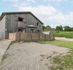 An exterior view of a wooden barn with fenced patio and gravel driveway at Top Lodge in Llanvair-Discoed near Penhow