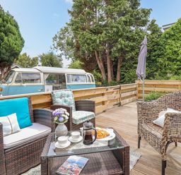 An outdoor wooden deck with wicker chairs a glass coffee table with coffee cups and croissants and a vintage blue and white van in the background at The Old Post Office in Llanelian near Old Colwyn