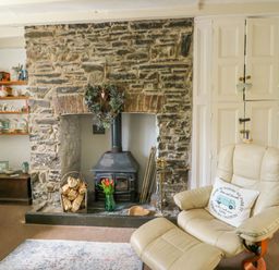 A living room with a stone fireplace wood stove and cream armchair at The Old Post Office in Llanelian near Old Colwyn