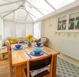 A dining area with a wooden table set with blue bowls and plates a sofa and armchair in a conservatory at The Old Post Office in Llanelian near Old Colwyn