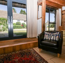 A sitting area with a black armchair with a pillow near glass doors and a window at Nympy Cottage in Nympsfield near Nailsworth