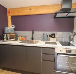 A kitchen with a sink, microwave, toaster, kettle, stovetop, oven, and utensils in containers at Daffodil in Llangadfan