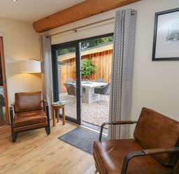 A sitting area with two brown leather chairs a small wooden side table and a sliding glass door leading to an outdoor patio at Daffodil in Llangadfan