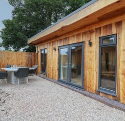 An outdoor patio area with a table and chairs next to a wooden building with glass doors and windows at Rhosyn in Llangadfan