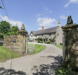 A stone house with a tiled roof behind a white gate and stone wall at Pentre Hall Bronygarth near Chirk