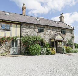 Stone and timber house with bushes and flowers in front and gravel driveway at Pentre Hall in Bronygarth near Chirk